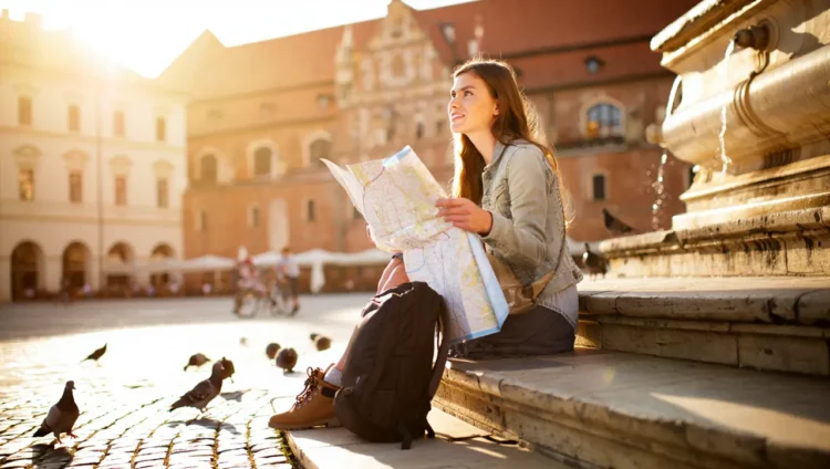 Young female traveler with backpack holding a paper map in a historic city square